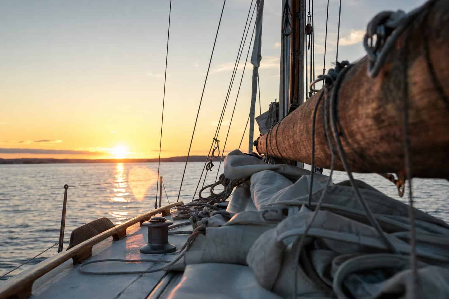 Blick über den Baum eines Segelboots auf den Sonnenuntergang über dem Wasser