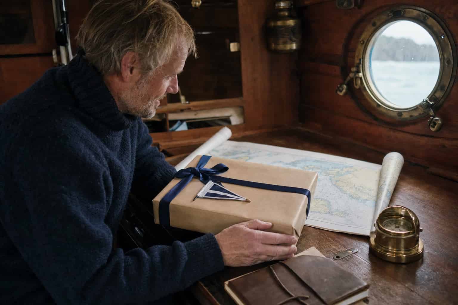 Mann öffnet ein verpacktes Geschenk in einer Bootskajüte